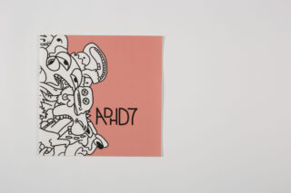 Ein quadratisches Heft mit lachsrosa Einband, abstrakten schwarz-weißen Kritzeleien auf der linken Seite und dem Text „APHID7“ in Schwarz auf der rechten Seite.