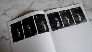 Auf einem offenen Buch auf einer Marmoroberfläche ist eine Fotoserie zu sehen, die einen Koch mit weißer Mütze und Schürze zeigt, der in einer Küche mit Teig arbeitet.