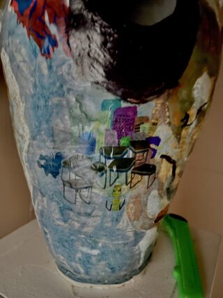 Eine Keramikvase mit einem abstrakten, farbenfrohen Muster aus überlappenden Formen und einem grünen Universalmesser neben dem Sockel.