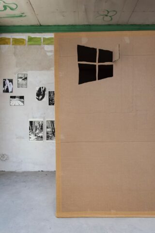 Eine große Papptafel mit einem Ausschnitt, der an ein Fenster erinnert, steht vor einer mit Schwarz-Weiß-Fotografien und Gemälden dekorierten Wand.