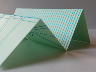 Nahaufnahme von gefaltetem Papier mit blauen Linien und Zeichnungen, die in dreieckigen Spitzen auf einer flachen Oberfläche angeordnet sind.