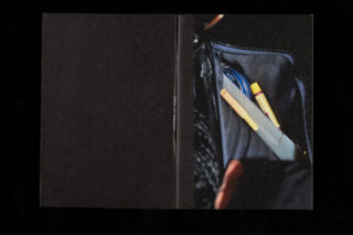 Eine Nahaufnahme einer offenen Taschentasche, die einen Kamm, einen gelben Lippenpflegestift und einen blauen Gegenstand enthält, wobei der Rest des Bildes größtenteils schwarz ist.