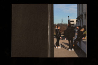 Eine Gruppe von vier Personen steht und sitzt an einem sonnigen Tag auf einem Felsvorsprung im Freien in der Nähe eines Gebäudes und unterhält sich.