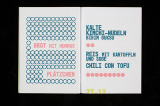 Ein aufgeschlagenes Buch zeigt ein zweisprachiges Menü auf Deutsch, auf dem „Brot mit Hummus“, „Plätzchen“, „Kalte Kimchi-Nudeln“, „Reis mit Kartoffeln und Soße“ und „Chili con Tofu“ aufgeführt sind.