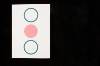 Eine weiße Karte mit drei Formen: einem rosafarbenen Kreis in der Mitte und zwei blau umrandeten Kreisen, einer darüber und einer darunter, auf schwarzem Hintergrund.