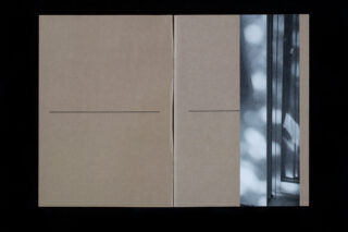 Ein offenes Buch mit zwei leeren braunen Seiten mit dünnen horizontalen Linien und einem teilweisen Schwarzweißfoto eines Fensters mit hellen Flecken auf der rechten Seite.