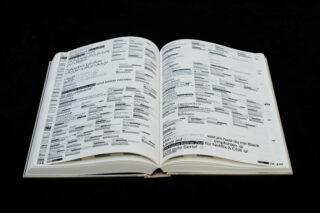 Ein offenes Buch mit Seiten mit dichtem, schwarz-weiß gedrucktem Text und grafischen Elementen auf schwarzem Hintergrund.