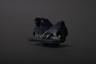 Eine dunkle, abstrakte und gezackte Skulptur mit schattigen und geschichteten Texturen steht vor einem schlichten grauen Hintergrund.