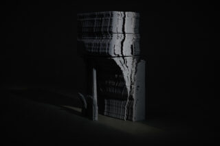 Eine vertikal gestapelte, abstrakte graue Skulptur mit wellenförmigen, verzerrten Linien steht vor einem dunklen Hintergrund.