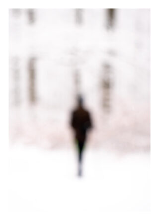 Eine verschwommene Silhouette einer Person, die draußen in einem verschneiten Waldgebiet mit undeutlichen Bäumen im Hintergrund steht.