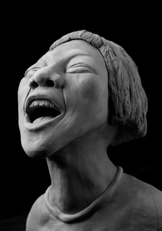 Eine Graustufenskulptur einer Person mit kurzen Haaren und geschlossenen Augen, weit geöffnetem Mund, als würde sie singen oder schreien, vor einem schwarzen Hintergrund.