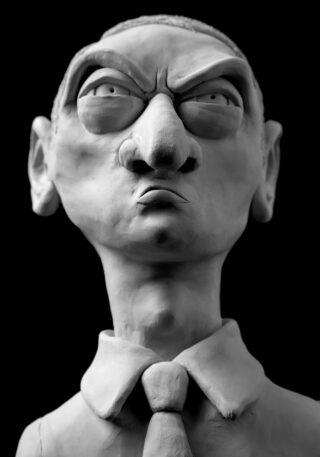Ton-Skulptur eines Mannes mit übertriebenem Stirnrunzeln, markanter Nase und gerunzelter Stirn, der ein Hemd mit Kragen und Krawatte trägt, auf schwarzem Hintergrund.