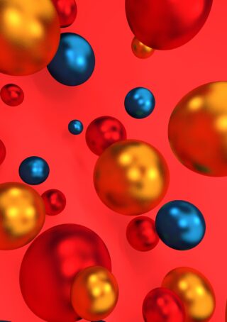 Metallisch rote, goldene und blaue Kugeln unterschiedlicher Größe schweben vor einem leuchtend roten Hintergrund.