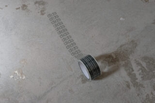 Eine Rolle transparentes Klebeband, das auf einer Betonoberfläche abgerollt ist und über die gesamte Länge das Wort „dida“ in wiederholten Abständen aufgedruckt ist.