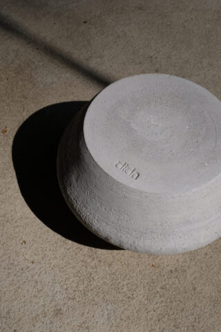 Eine graue, strukturierte Schüssel steht verkehrt herum auf einer Betonoberfläche und wirft einen dunklen Schatten. Auf dem Boden der Schüssel ist das Wort „Elicia“ eingeprägt.