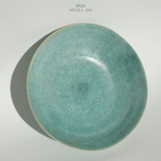 Ein runder, flacher, türkisfarbener Keramikteller mit gesprenkelter Textur wird vor einem schlichten, hellen Hintergrund fotografiert.