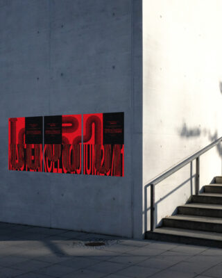 Rote und schwarze Poster mit abstrakten Mustern hängen im Sonnenlicht auf einer weißen Betonwand neben einem Geländer und Außentreppen.