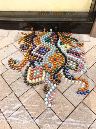 Bunte Kaffeekapseln, die in einem wirbelnden Muster auf einem gefliesten Gehweg vor einem Fenster angeordnet sind.