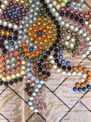 Ein Mosaikkunstwerk auf Fliesenboden aus bunten Kaffeekapseln, die in einem dekorativen Muster angeordnet sind.