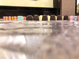 Reihen verschiedener Pralinen in unterschiedlichen Farben und Mustern sind ordentlich auf einer reflektierenden Oberfläche angeordnet.