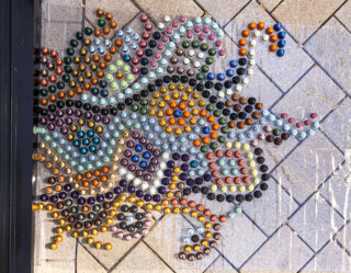 Ein farbenfrohes, abstraktes Mosaikmuster aus angeordneten Kaffeekapseln auf einer gefliesten Außenfläche.