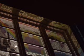 Buntglasfenster mit farbenfrohen abstrakten Mustern, teilweise beleuchtet, nachts aus der Innenperspektive betrachtet.