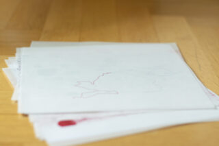 Auf einer Holzoberfläche liegt ein kleiner Stapel weißer Blätter mit schwachen roten und blauen Strichzeichnungen.