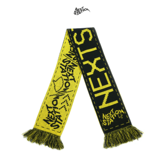 Ein gelb-schwarzer Schal mit dem Text „NEXT STATION“ und abstrakten Designs, mit Fransenenden und kräftigen Kontrastmustern.