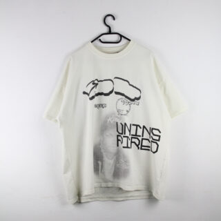 Weißes, übergroßes T-Shirt auf einem Kleiderbügel mit schwarzen abstrakten Grafiken, Text und einem schwachen Bild einer Person auf der Vorderseite, vor einer schlichten weißen Wand.