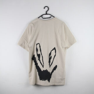 Ein beiges T-Shirt hängt auf einem schwarzen Kleiderbügel und hat auf der Rückseite ein großes, abstraktes schwarzes Grafikdesign.