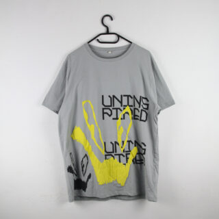 Ein graues T-Shirt mit abstrakten gelben und schwarzen Designs und dem teilweise lesbaren Text „UNINS PIRED“ auf der Vorderseite, das auf einem schwarzen Kleiderbügel vor einer weißen Wand hängt.