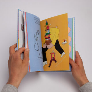 Hände halten ein bunt illustriertes Buch aufgeschlagen; die sichtbare Seite zeigt eine Person, die einen hohen Stapel Schüsseln und Teller trägt, gefolgt von einem kleinen Hund.