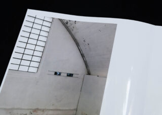 Ein Foto einer weißen Innenwand mit einem gitterartigen Fenster, einer gewölbten Decke und zwei kleinen rechteckigen Lüftungsöffnungen oder Paneelen, gedruckt auf Hochglanzpapier.