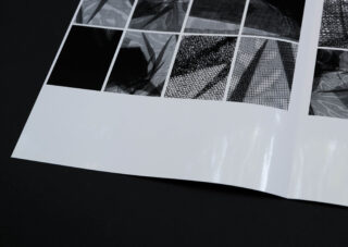 Auf einer dunklen Oberfläche liegt ein glänzendes Blatt Papier mit einem Raster aus abstrakten Schwarzweißbildern.