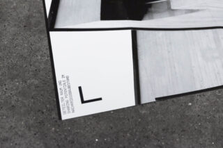 Eine Nahaufnahme einer gedruckten Architekturfotografie auf einer Betonoberfläche, die einen Teil eines Gebäudemodells zeigt, an dessen Unterkante deutscher Text aufgedruckt ist.