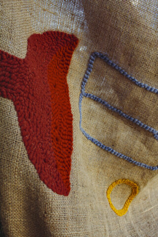 Ein Stück Sackleinenstoff mit abstrakten Formen, die mit rotem, blauem und gelbem Garn bestickt sind.