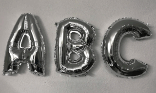 Drei metallisch silberne Folienballons in Form der Großbuchstaben A, B und C sind an einer schlichten weißen Wand befestigt.