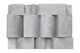 Eine geometrische Anordnung großer rechteckiger und quadratischer Betonblöcke, die ungleichmäßig gestapelt sind und so eine strukturierte, dreidimensionale Wand bilden.