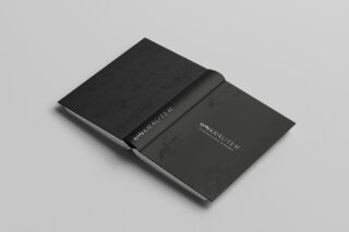 Ein offenes schwarzes Notizbuch mit botanischen Illustrationen und dem Wort „KRAUTER“ in Weiß auf beiden Seiten, platziert auf einer hellgrauen Oberfläche.