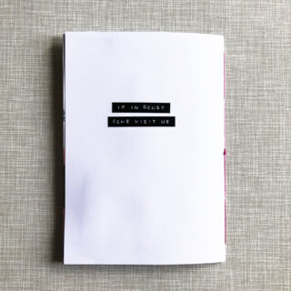 Ein weißes Heft auf strukturierter Oberfläche mit den Worten „IF IN DOUBT COME VISIT US“, die mit schwarzem Etikettenband auf den Umschlag gedruckt sind.