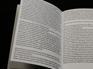 Ein offenes Buch zeigt zwei Seiten dicht gedruckten deutschen Text in schwarzer Schrift auf weißem Papier, fotografiert vor einem dunklen Hintergrund.