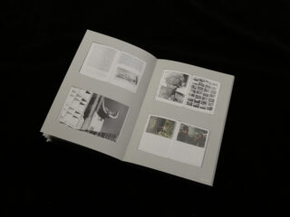 Ein aufgeschlagenes Buch auf schwarzem Untergrund zeigt auf beiden sichtbaren Seiten Schwarzweißfotos, Text und Fotokontaktabzüge.