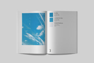 Offenes Buch mit einem Foto eines blauen Himmels mit Wolken auf der linken Seite und drei blauen und grauen Farbmustern mit Beschriftungen auf der rechten Seite.