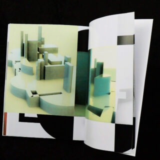 Ein offenes Buch, das abstrakte Architekturmodelle in geometrischen Formen und gedämpften Farben vor einem schwarzen Hintergrund zeigt.