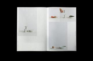 In einer aufgeschlagenen Zeitschrift sind minimalistische Fotos von weißem Geschirr, darunter Schüsseln und eine Tasse, mit vereinzelten Speisen und einer Hand, die aus einer Karaffe einschenkt, zu sehen.