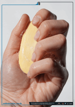 Eine Nahaufnahme einer Hand, die ein nasses Stück gelbe Seife greift, mit sichtbaren Seifenblasen an den Fingern und der Handfläche.