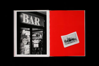 Ein offenes Buch zeigt auf der linken Seite ein Schwarzweißfoto eines Bareingangs und auf der rechten Seite ein kleines Vintage-Foto auf einem einfarbig roten Hintergrund.