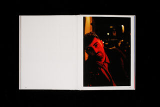 Ein offenes Buch zeigt eine leere weiße linke Seite und eine rechte Seite mit dem Porträt eines Mannes in einer dunklen, von rotem Licht beleuchteten Umgebung.