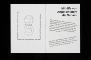 Ein aufgeschlagenes Buch zeigt auf der linken Seite die Skizze einer Toilette und auf der rechten Seite einen deutschen Text zum Thema Scham und Angst.
