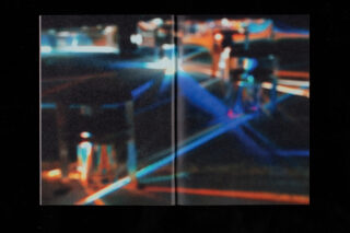 Ein verschwommenes Bild mit bunten Lichtstrahlen und Reflexionen, die über einen dunklen, undeutlichen Hintergrund mit einigen schattenhaften Figuren oder Objekten verlaufen.